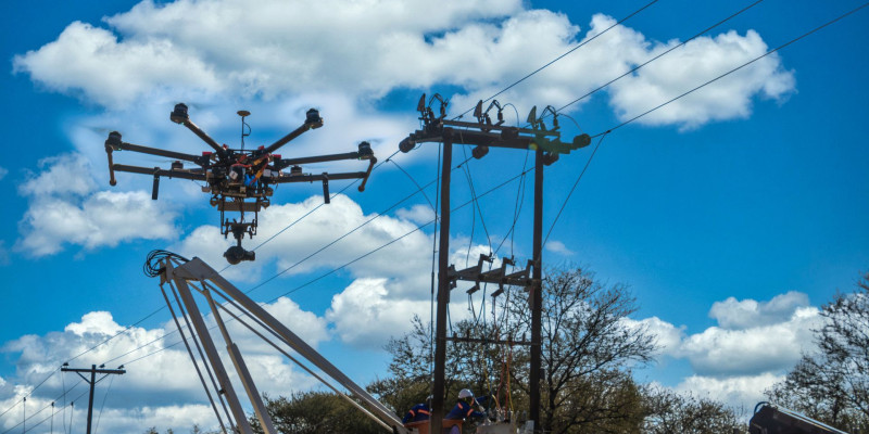 Hexacopter inspiziert eine Freileitung, Monteure arbeiten am Mast